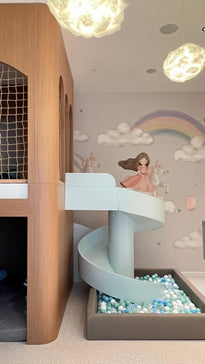 Unicorn üzerinde el çizimi bir kız çocuğu, bulutlar ve gökkuşağıyla sakin tonlu çocuk odası duvar kağıdı; önünde oyun evi ve top havuzu