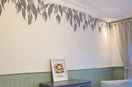 Gray-leaf trailing vine wall decal hanging from the ceiling molding in a nursery, above green wainscoting and a dresser with a lion print