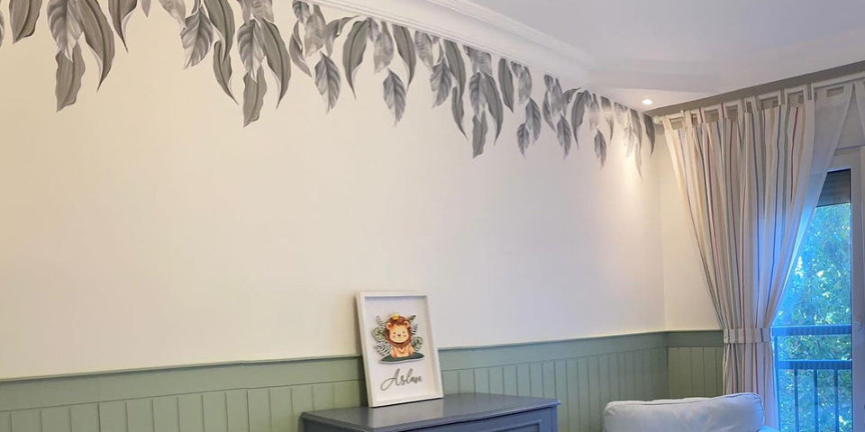 Gray-leaf trailing vine wall decal hanging from the ceiling molding in a nursery, above green wainscoting and a dresser with a lion print