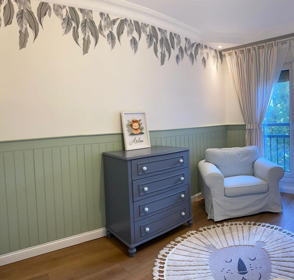 Bebek odasında tavan kartonpiyerinden sarkan gri yapraklı sarmaşık duvar stickerı, altında yeşil lambri ve gri şifonyer