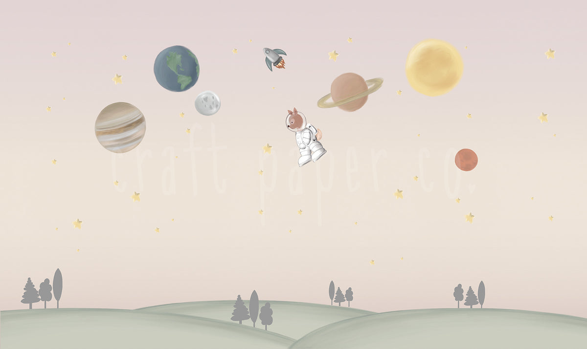 Ceylan Astronot Duvar Kağıdı; pembe-bej gökte gezegenler, roket ve astronot ceylan, altta yeşil tepeler | Craft Paper Co
