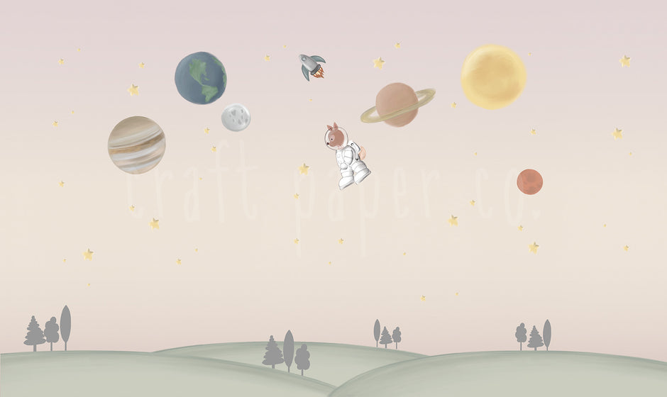 Ceylan Astronot Duvar Kağıdı; pembe-bej gökte gezegenler, roket ve astronot ceylan, altta yeşil tepeler | Craft Paper Co