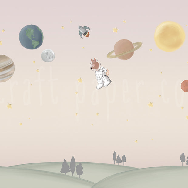 Ceylan Astronot Duvar Kağıdı; pembe-bej gökte gezegenler, roket ve astronot ceylan, altta yeşil tepeler | Craft Paper Co